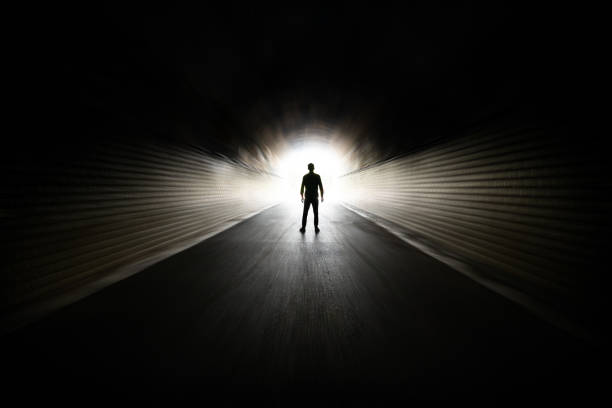 uomo che cammina in un tunnel buio - luce alla fine del tunnel foto e immagini stock