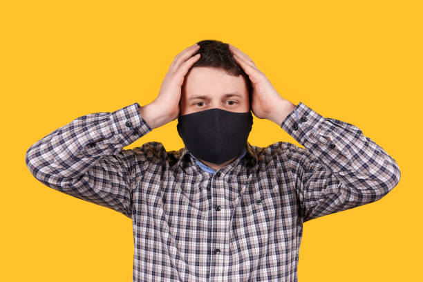 istock Man in black face mask holding his head with hands, isolated on orange background. 1223361194