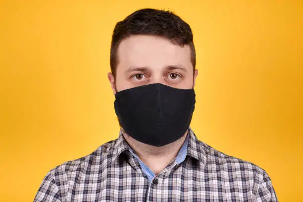 Photo of Man in black face mask, isolated on orange background.