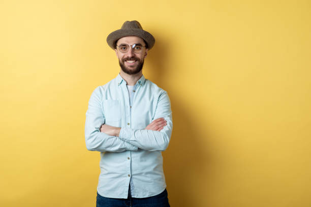 istock Man wearing in casual clothing, glasses and hat standing folded hands and cheeerful smiling against an yellow background. Confidence emotion 1223361293
