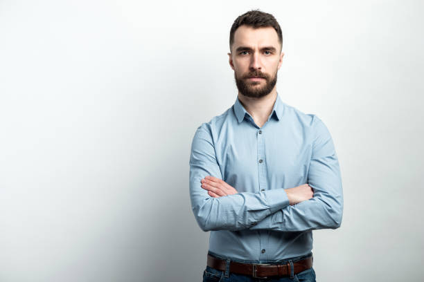 istock Serious guy in blue shirt stands folded hands and posing against a white studio background 1223361392