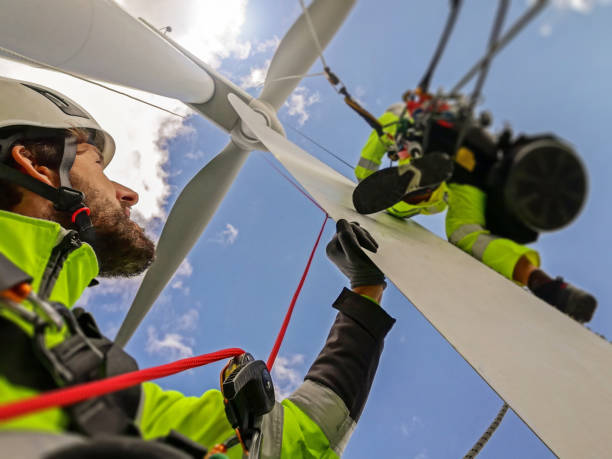 View from under on two rope access technicians working on blade of wind turbine high up stock photo