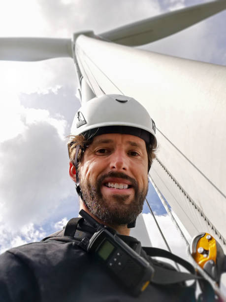 carismatici tecnici di accesso alla corda con barba, radio e casco si sono selfie sotto turbina eolica con lama e sorridente. - working windmill foto e immagini stock