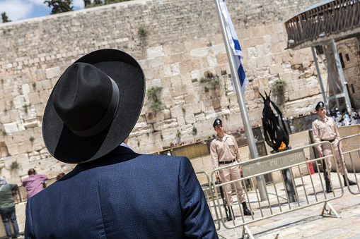 Jerusalem, Israel, May 8, 2019: Orthodox jew looking at israeli soldiers standing at attention by half-mast lowering Israeli flag, remembering to Israel's military heroes on Israel's Memorial Day, at Wailing Wall in Jerusalem Old City, Israel
