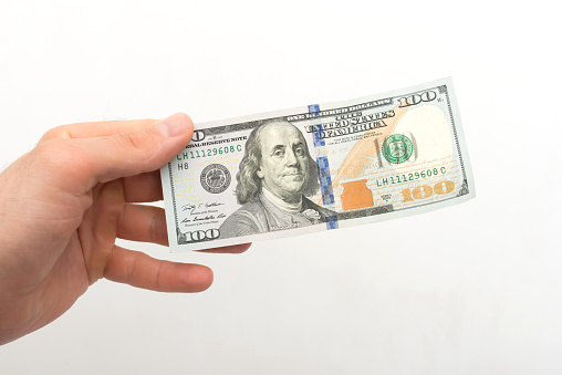 Hand holds a 100 dollar bill on a white background