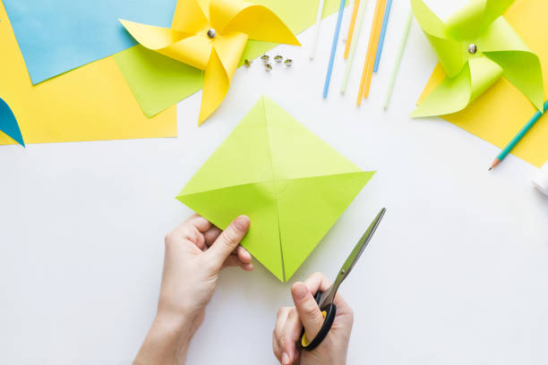 istock How to make paper green windmill toy with children at home. Step by step instructions. Hands making DIY summer project. Step 5. Cut sheet in lines to circle in center, getting half-cut triangles. 1223364323