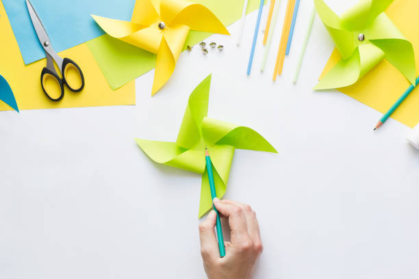 istock How to make paper green windmill toy with children at home. Step by step instructions. Hands making DIY summer project. Step 9. Mark center of resulting figure, capturing all the edges of triangles. 1223364360