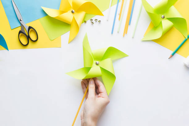 istock How to make paper green windmill toy with children at home. Step by step instructions. Hands making DIY summer project. Top view. Step 12. Enjoy ready toy. 1223364397