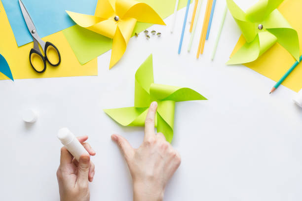 istock How to make paper green windmill toy with children at home. Step by step instructions. Hands making DIY summer project. Top view. Step 8. Glue remaining corners, overlaying each other. 1223364425