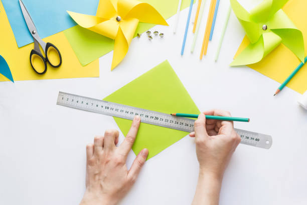 istock How to make paper green windmill toy with children at home. Step by step instructions. Hands making DIY summer project. Top view. Step 2. Draw line between opposite corners of square. 1223364503