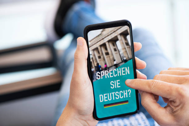 text do you speak German in German in a smartphone closeup of a young caucasian man, wearing casual clothes, sitting in a chair indoors, having his smartphone in his hand with the text do you speak German written in German in its screen german language photos stock pictures, royalty-free photos & images