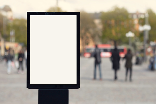 A modern blank poster on a city square with people in the background.