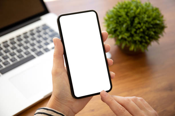 istock female hands holding phone with isolated screen laptop in office 1223367775
