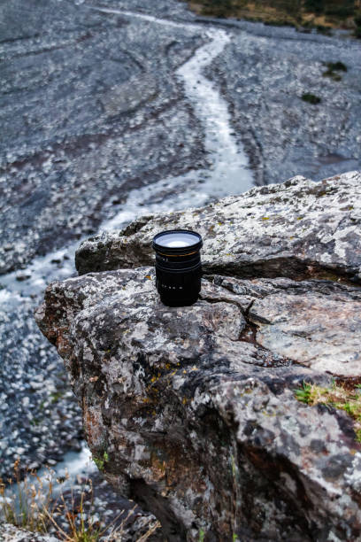 istock DSLR camera lens on the edge of a stone overlooking a mountain river 1223371064