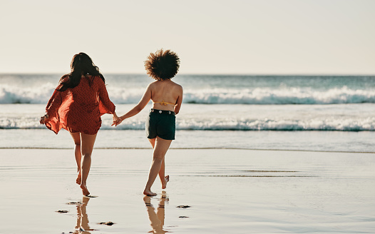 Full length shot of two unrecognizable friends standing together and holding hands while walking on the beach