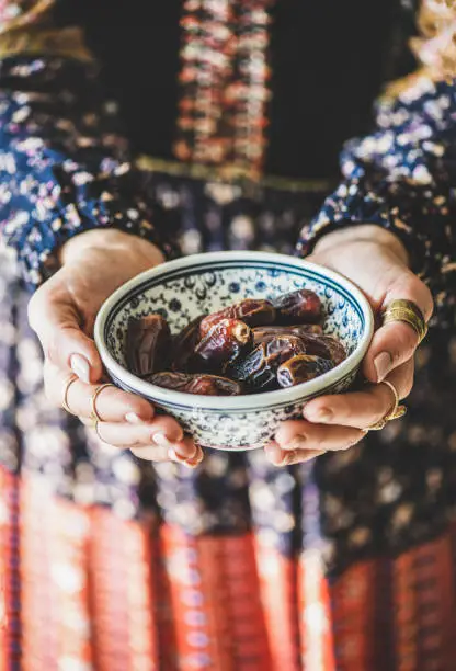 Woman in oriental dress holding bowl of dates in hands for Ramadan iftar evening meal and fasting month. Ramazan Muslim fasting food and islamic Middle East tradition