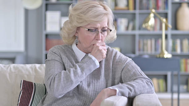 istock Sick Old Woman Sitting on Sofa and Coughing 1223373639