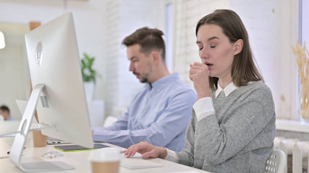 istock Creative Woman Working on Desktop and Coughing in Office 1223373830