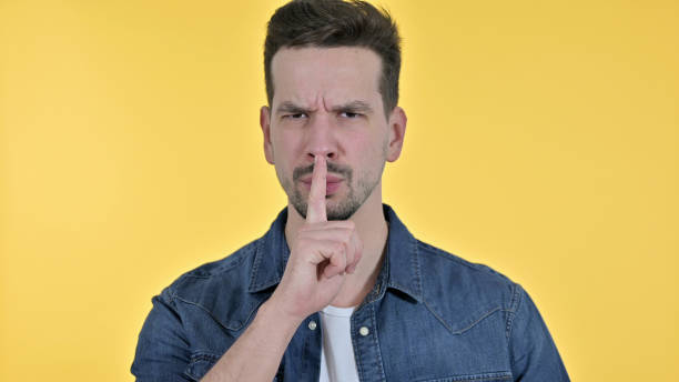 istock Young Man putting Finger on Lips, Yellow Background 1223375979