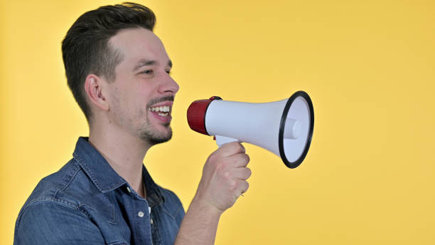 istock Young Man making Announcement on Loudspeaker, Yellow Background 1223376524
