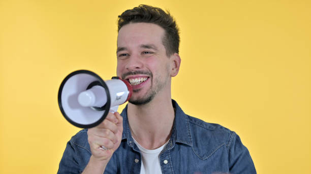 istock Young Man Talking on Loudspeaker, Yellow Background 1223376569