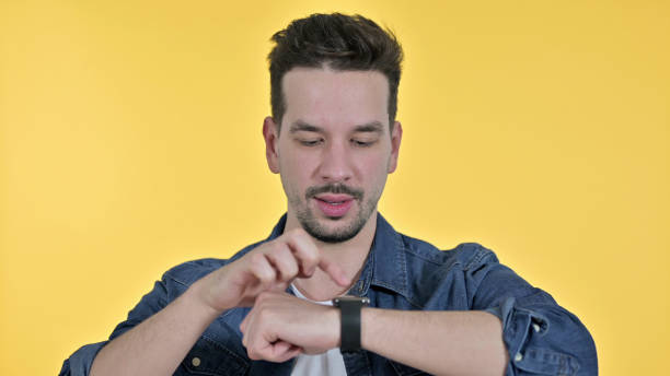 istock Portrait of Professional Young Man using Smartwatch, Yellow Background 1223376678