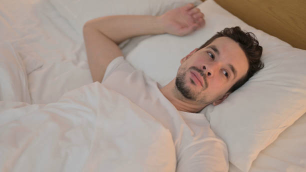 istock Tired Young Man Trying to Sleep in Bed 1223377378