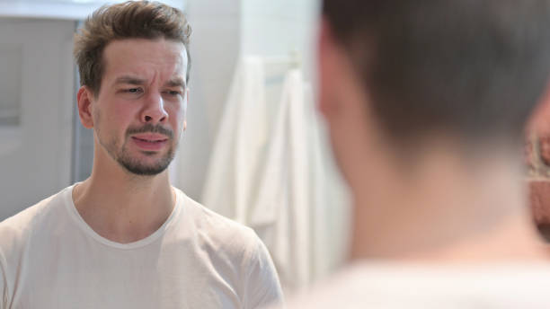 istock Upset Young Man looking at Face in Mirror 1223377670