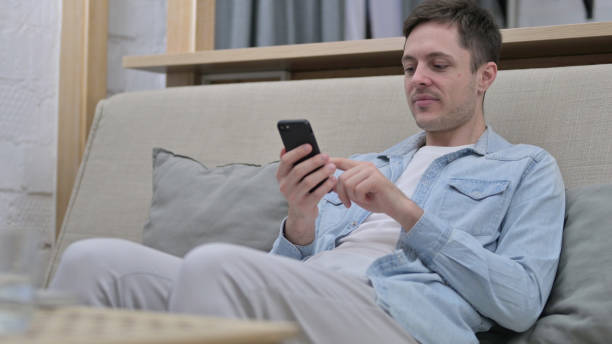istock Relaxed Young Man using Smartphone in Living Room 1223377987