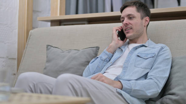 istock Young Man Sitting on Sofa and Talking on Smartphone 1223378575