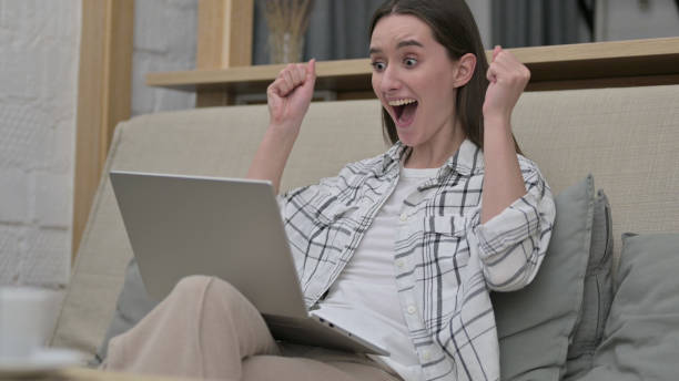 istock Ambitious Young Woman Celebrating Success on Laptop on Sofa 1223378986