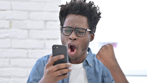 istock Young African Man Celebrating Success on Smartphone 1223380372
