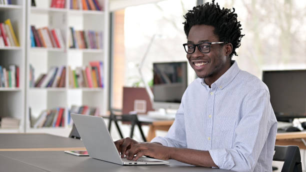 istock African Man Smiling at Camera while Working on Laptop 1223380881