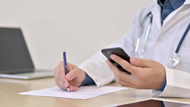 istock Doctor using Smartphone Writing on Paper Close up 1223381189