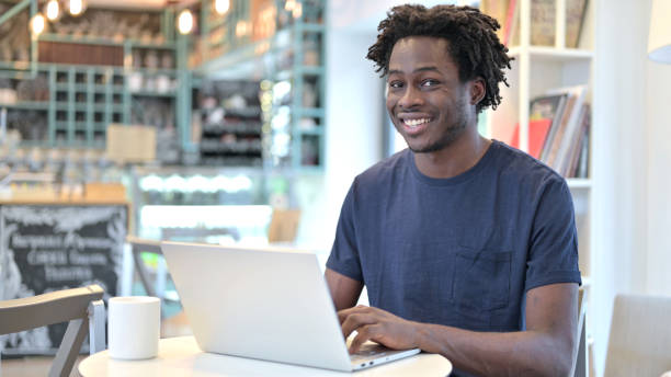 istock African Man with Laptop Smiling at Camera in Cafe 1223381609