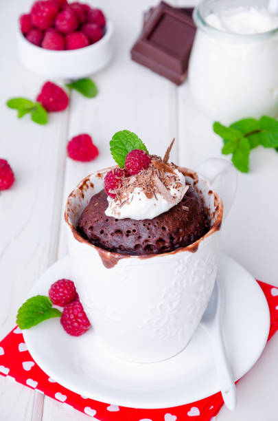 istock Chocolate mug cupcake with whipped cream, chocolate chips and fresh raspberries on a white wooden background. 1223383711