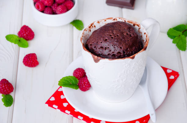istock Chocolate mug cupcake with whipped cream, chocolate chips and fresh raspberries on a white wooden background. 1223383724