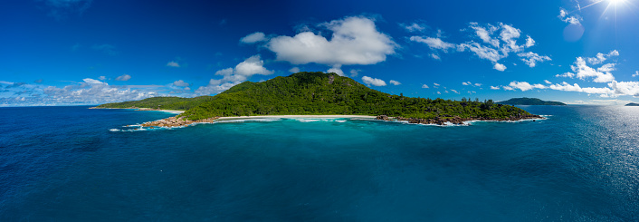 beautiful panoramic aerial view of a beach on the island La Digue on Seychelles with beautiful waves and a clear blue sky with some clouds wider view