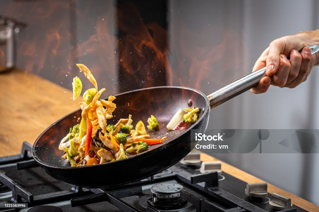 Chef tossing flaming vegetable Chef tossing flaming vegetable in a frying pan. Cooking Stock Photo