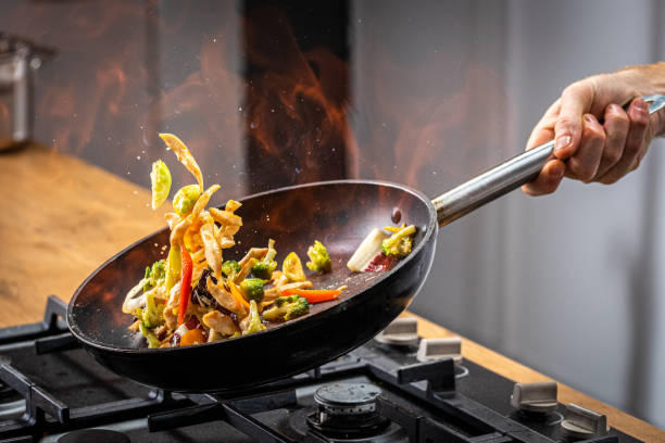 Chef tossing flaming vegetable Chef tossing flaming vegetable in a frying pan. pan stock pictures, royalty-free photos & images