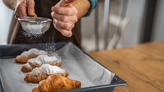 Photo of a chef using a strainer to sprinkle powdered sugar on freshly baked croissants.
