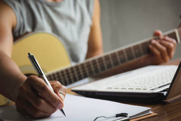 Composer holding pencil and writing lyrics in paper. Musician playing acoustic guitar. stock photo