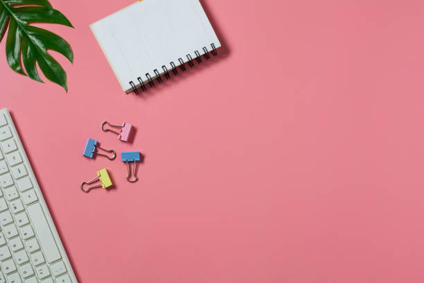 istock Top view with the keyboard and notebook on pink background. Cluttered office desk background. 1223385068