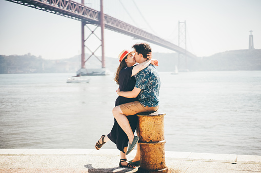 Romantic couple kissing in front of the bridge called April 25 in Lisbon in Portugal at sunny summer day.