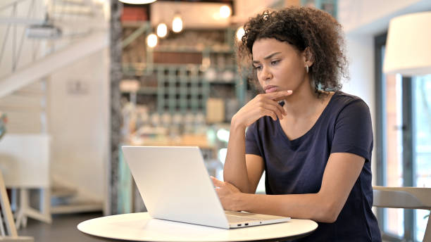mulher jovem africana pensativa usando laptop no café - pensive women business mature adult - fotografias e filmes do acervo