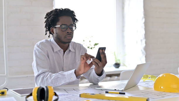 ingénieur d’architecture africain utilisant smartphone dans l’office - men mail manual worker human hand photos et images de collection