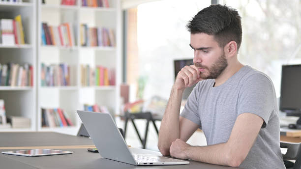 istock Pensive Young Man Reading on Laptop in Office 1223386066