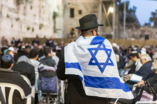 Jerusalem, Israel, May 8, 2019: Jewish men waiting for praying at Western Wall, Wailing Wall, Kotel, one israeli jew wearing an Israeli flag in Jerusalem Old City, Israel