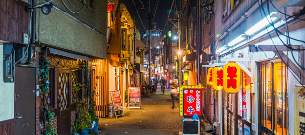 People strolling through the neon drenched alleyways of restaurants and bars at night in the Juso district of Osaka, Japan’s vibrant second city.