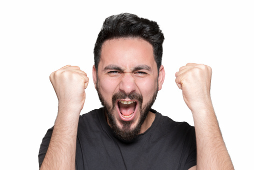 Portrait of happy young man cheering by shaking fist over white background. Horizontal composition. Studio shot.